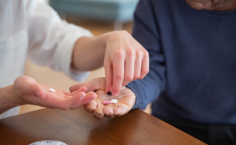 Caregiver placing pills into an older adult’s hand